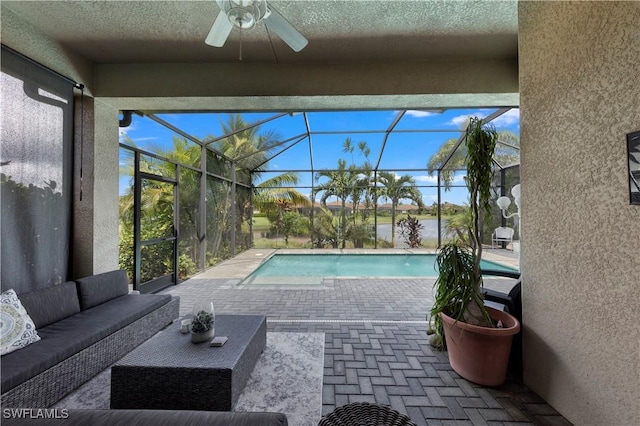 view of pool featuring outdoor lounge area, a patio, glass enclosure, and ceiling fan