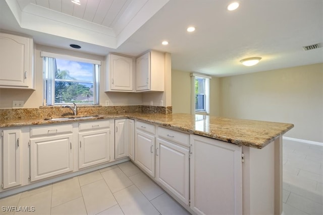 kitchen with light stone counters, sink, white cabinets, kitchen peninsula, and a raised ceiling