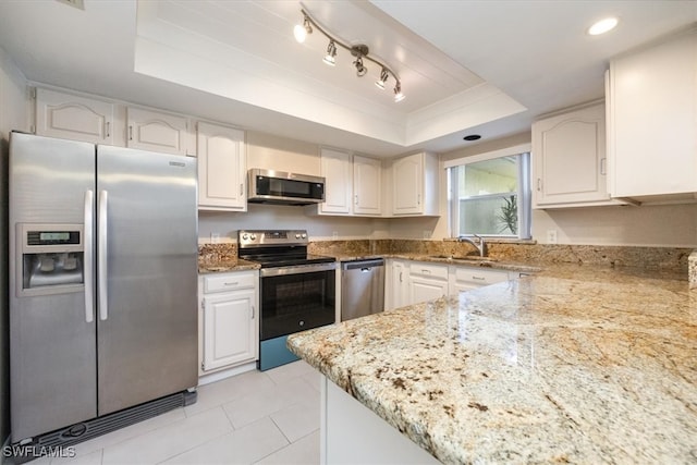 kitchen with a raised ceiling, light stone countertops, stainless steel appliances, and white cabinets