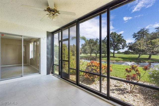 unfurnished sunroom featuring ceiling fan, a water view, and a healthy amount of sunlight