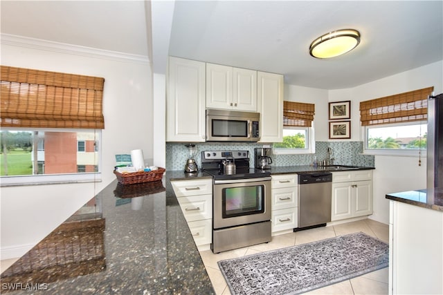 kitchen featuring decorative backsplash, appliances with stainless steel finishes, dark stone counters, white cabinetry, and light tile patterned flooring