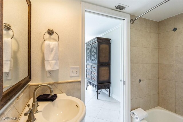 bathroom featuring tile patterned floors, tiled shower / bath combo, sink, and tile walls