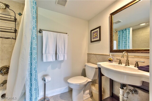 bathroom with tile patterned floors, toilet, and tile walls