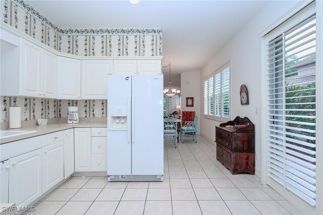 kitchen featuring white fridge with ice dispenser, a chandelier, white cabinetry, light tile patterned floors, and decorative light fixtures