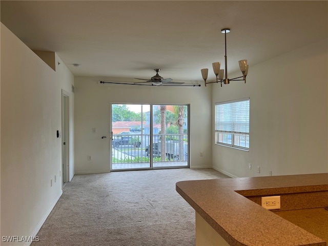 unfurnished living room featuring ceiling fan with notable chandelier and light colored carpet