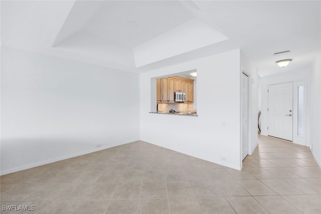 unfurnished living room featuring light tile patterned flooring and a tray ceiling