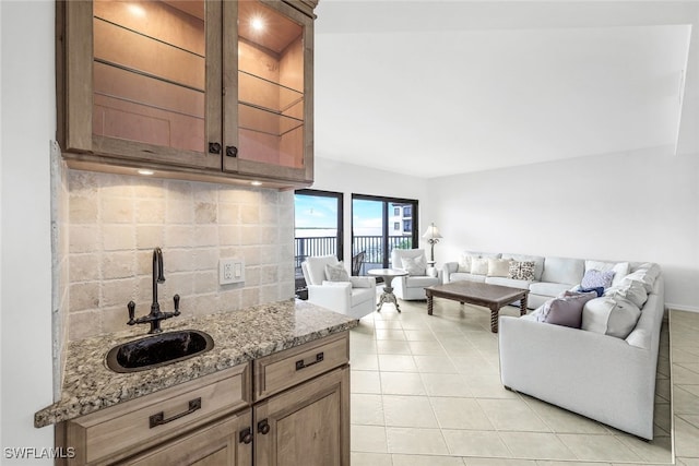 kitchen with tasteful backsplash, light tile patterned flooring, sink, and light stone counters