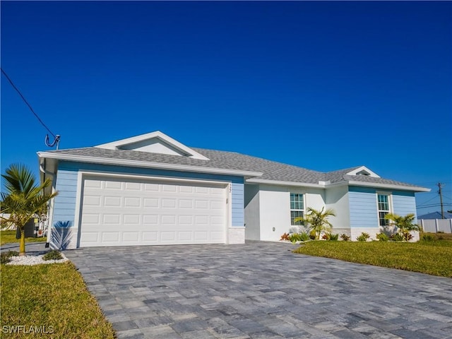 ranch-style home featuring a front yard, central AC, stucco siding, decorative driveway, and an attached garage