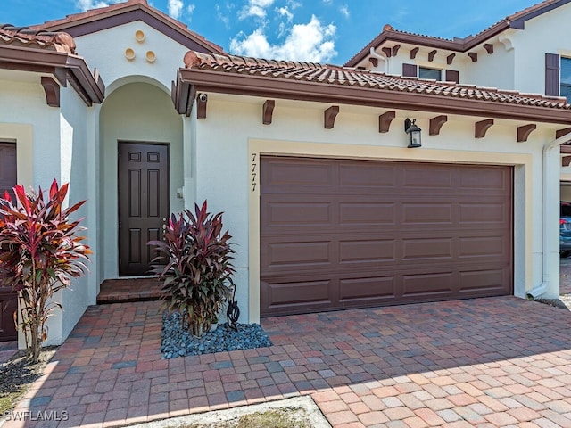 mediterranean / spanish-style house with a garage, stucco siding, and decorative driveway