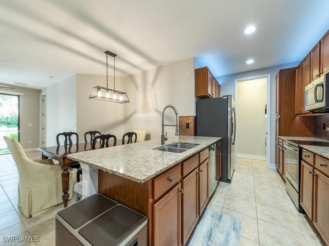 kitchen with hanging light fixtures, an island with sink, stainless steel appliances, sink, and light stone counters