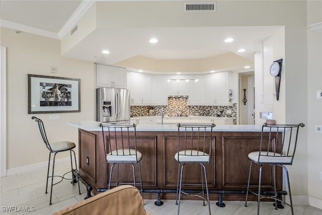 kitchen with a breakfast bar, white cabinets, stainless steel fridge, backsplash, and ornamental molding