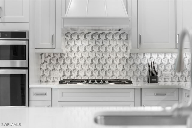 kitchen featuring decorative backsplash, premium range hood, and white cabinetry