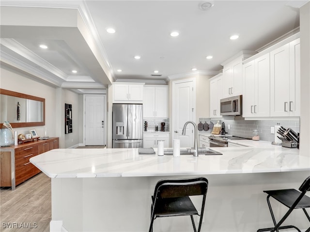 kitchen with light hardwood / wood-style flooring, stainless steel appliances, white cabinetry, kitchen peninsula, and a breakfast bar area