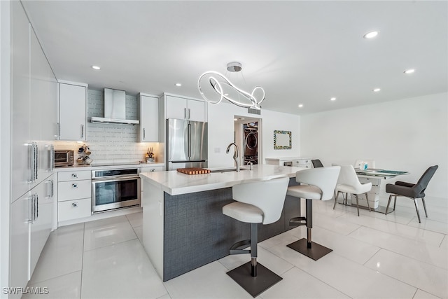 kitchen featuring a notable chandelier, white cabinets, hanging light fixtures, wall chimney exhaust hood, and stainless steel appliances