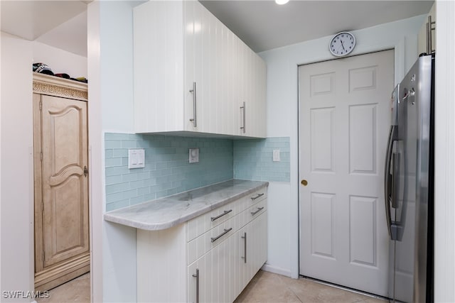 kitchen featuring white cabinets, tasteful backsplash, light tile patterned floors, and stainless steel refrigerator