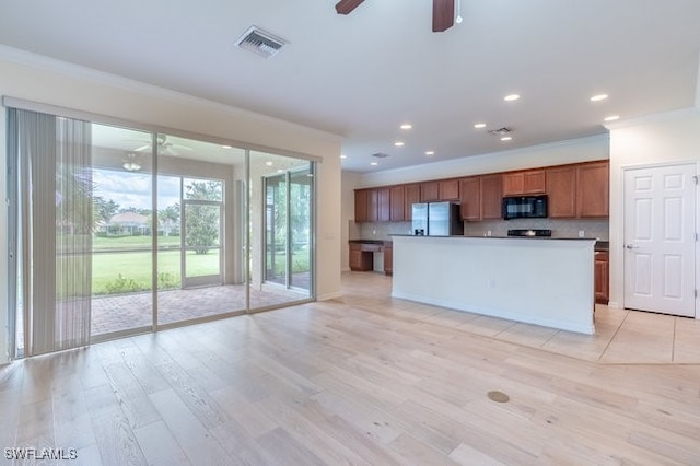 kitchen featuring ceiling fan, stainless steel fridge, a center island with sink, light wood-type flooring, and decorative backsplash