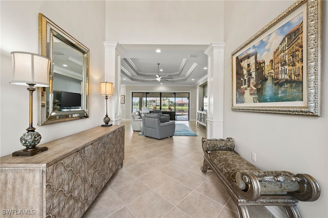 hall featuring ornamental molding, a tray ceiling, decorative columns, and light tile patterned floors