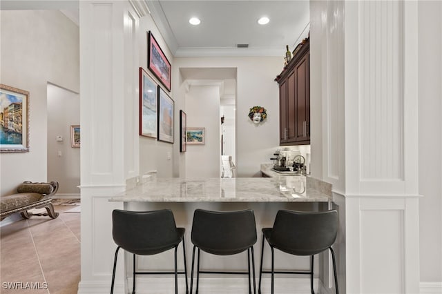 kitchen featuring dark brown cabinets, light stone counters, kitchen peninsula, and a breakfast bar