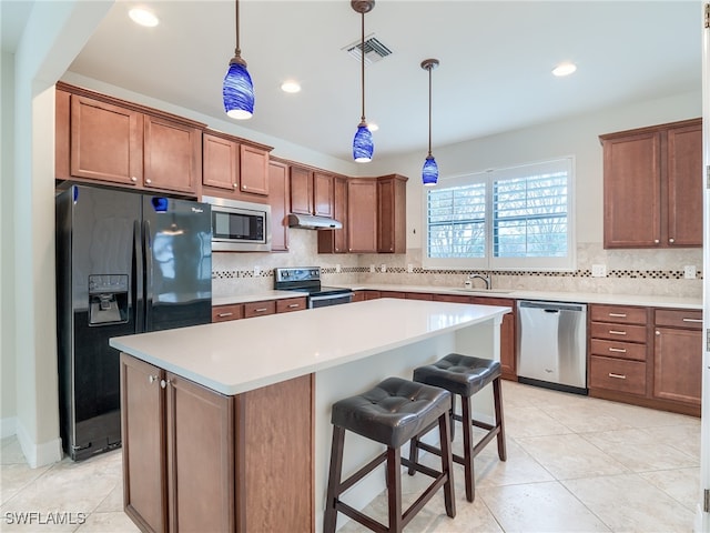 kitchen with a breakfast bar area, black appliances, decorative light fixtures, and a kitchen island