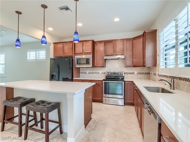 kitchen with appliances with stainless steel finishes, sink, pendant lighting, decorative backsplash, and a breakfast bar area