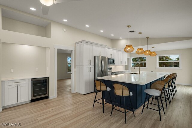 kitchen with hanging light fixtures, sink, white cabinets, beverage cooler, and stainless steel appliances