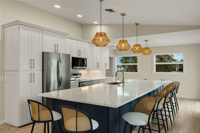 kitchen with light stone countertops, appliances with stainless steel finishes, a spacious island, white cabinetry, and pendant lighting