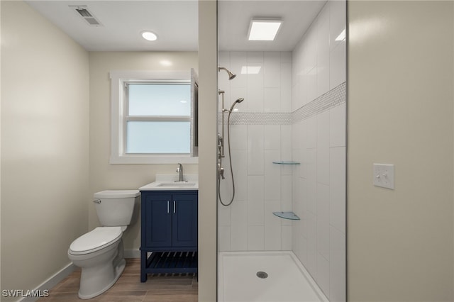 bathroom featuring visible vents, toilet, a tile shower, wood finished floors, and baseboards