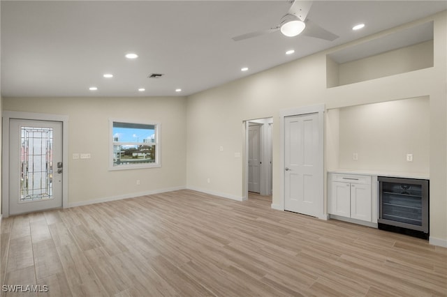 unfurnished living room with indoor bar, vaulted ceiling, light wood-type flooring, ceiling fan, and wine cooler