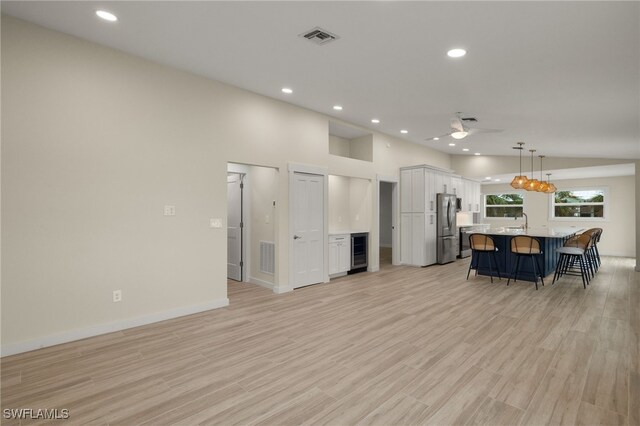 kitchen with white cabinets, light wood-type flooring, pendant lighting, beverage cooler, and stainless steel fridge