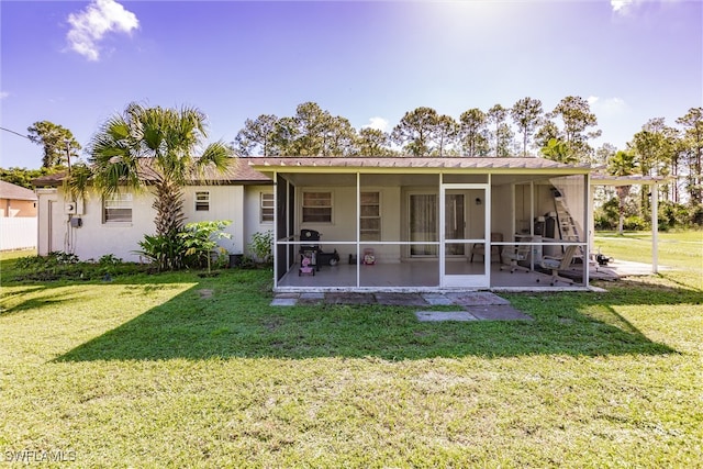 rear view of property featuring a sunroom, a lawn, and a patio area