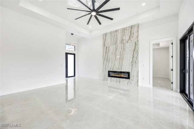 unfurnished living room featuring baseboards, a ceiling fan, a towering ceiling, a tray ceiling, and a fireplace