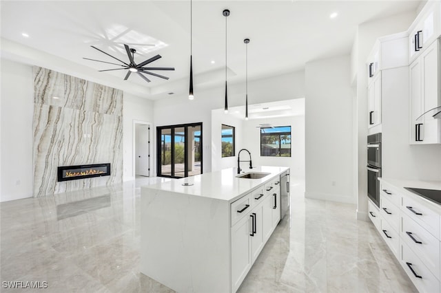 kitchen featuring a kitchen island with sink, white cabinetry, open floor plan, and a sink