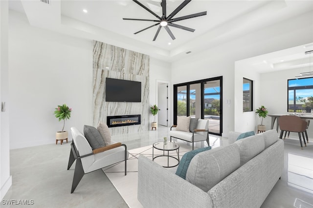 living room with ceiling fan, a raised ceiling, and a high end fireplace