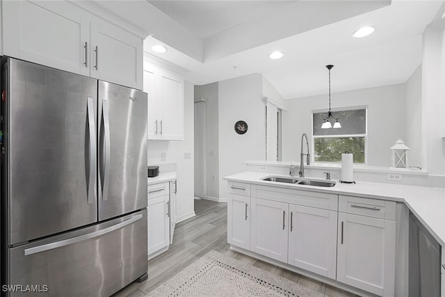 kitchen featuring stainless steel refrigerator, light wood-type flooring, sink, hanging light fixtures, and white cabinetry