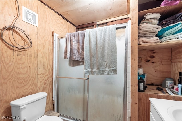 bathroom with wooden walls, toilet, vanity, and an enclosed shower