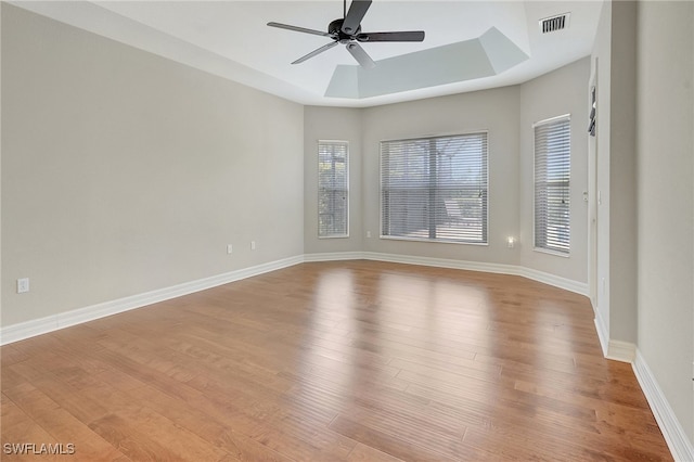 spare room featuring a raised ceiling, ceiling fan, and light hardwood / wood-style flooring