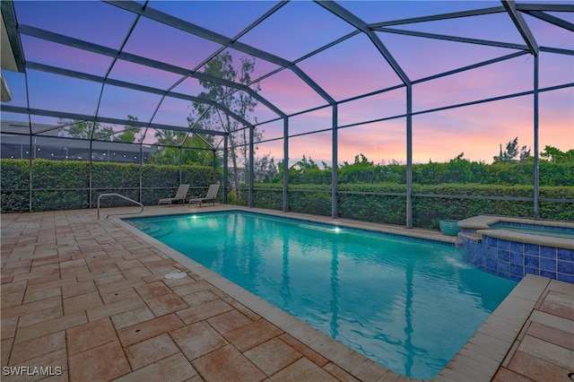 pool at dusk featuring glass enclosure, an in ground hot tub, pool water feature, and a patio