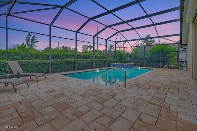 pool at dusk featuring an in ground hot tub, a patio area, and a lanai