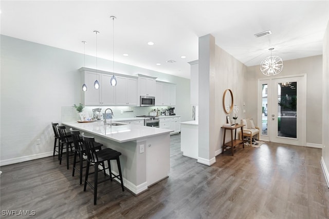 kitchen with dark wood-type flooring, hanging light fixtures, kitchen peninsula, a kitchen bar, and appliances with stainless steel finishes