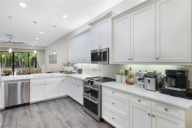 kitchen with white cabinets, appliances with stainless steel finishes, light wood-type flooring, sink, and decorative light fixtures