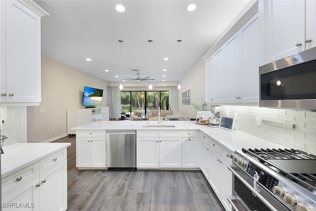 kitchen with kitchen peninsula, decorative light fixtures, appliances with stainless steel finishes, light hardwood / wood-style floors, and ceiling fan