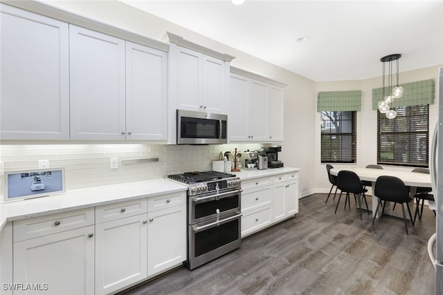 kitchen with appliances with stainless steel finishes, white cabinets, decorative light fixtures, and dark wood-type flooring