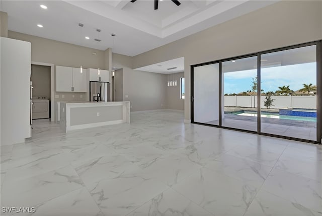 unfurnished living room with ceiling fan, beamed ceiling, and washer / dryer