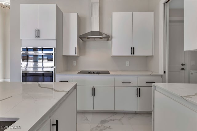 kitchen with black electric cooktop, stainless steel double oven, wall chimney range hood, and white cabinetry