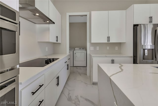 kitchen featuring light stone counters, wall chimney range hood, white cabinetry, stainless steel appliances, and washing machine and dryer