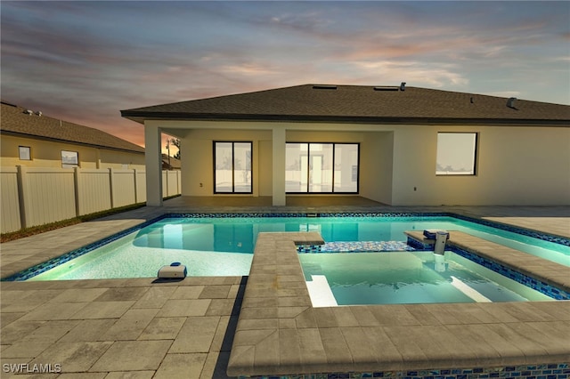 pool at dusk featuring an in ground hot tub and a patio