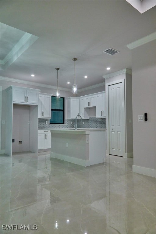 kitchen featuring decorative light fixtures, tasteful backsplash, a kitchen island with sink, and white cabinets