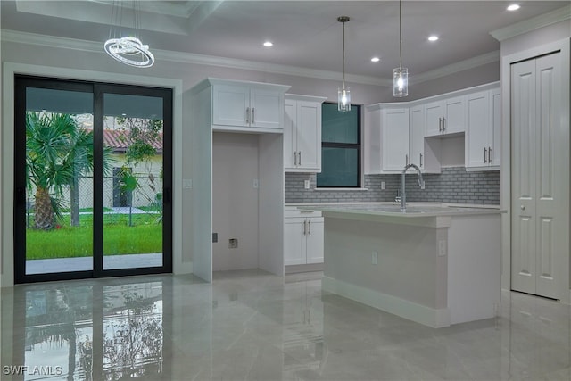 kitchen featuring an island with sink, white cabinetry, decorative light fixtures, and crown molding