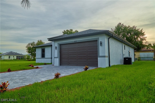 garage at dusk with a lawn and cooling unit