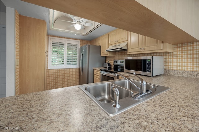 kitchen featuring a tray ceiling, sink, stainless steel appliances, light brown cabinets, and ceiling fan